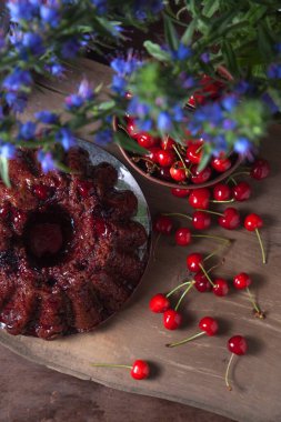 Koyu renk ahşap arka planda kompozisyon - tatlı kirazlı lezzetli çikolatalı pasta, kirazlı kirazlı kiraz kasesi, kaliteli çaydanlık ve güzel mavi çiçekli cam kavanoz.