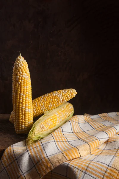 Several ears of ripe sweet corn on wooden background. Cobs with white and yellow grains. Fresh ear of corn with green leaves.