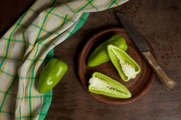Clay plate with whole and halves of green bell pepper (capsicum) known as sweet bell pepper, paprika and green kitchen towel on vintage wooden background. Vegetables collection.