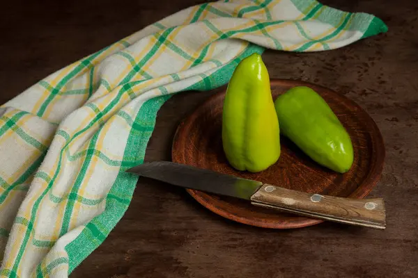 Clay plate with two whole green bell pepper (capsicum) known as sweet bell pepper, paprika and green kitchen towel on vintage wooden background. Vegetables collection.