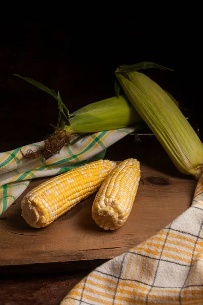 Two ears of ripe sweet corn and green towel on vintage wooden background. Cobs with white and yellow grains. Fresh ears of corn with green leaves on background.