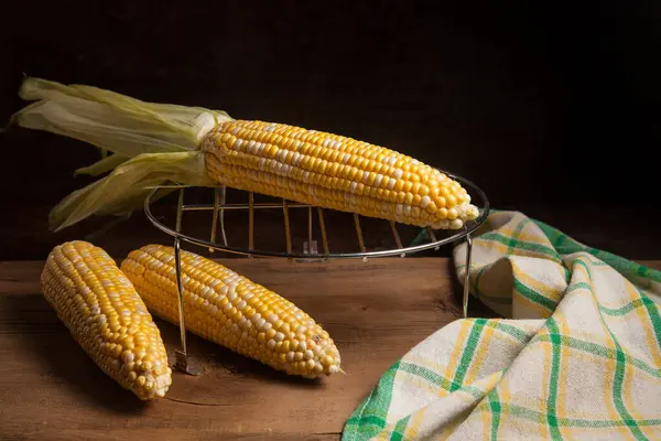 Several ears of ripe sweet corn and green towel on vintage wooden background. Cobs with white and yellow grains. Fresh ears of corn with green leaves on background.