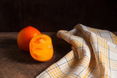 Kaliteli ahşap arka planda tam ve yarım porsiyon sulu sarı domates ve sarı havlu. Sebze koleksiyonu