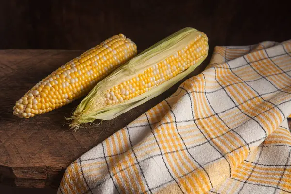 Two ears of ripe sweet corn on wooden background. Cobs with white and yellow grains. Fresh ear of corn with green leaves.