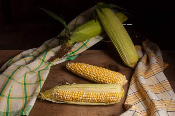 Two ears of ripe sweet corn with green leaves and green towel on vintage wooden background. Cobs with white and yellow grains.