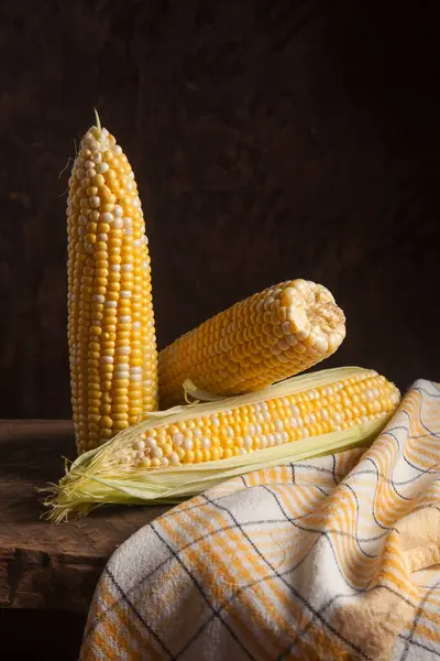 Several ears of ripe sweet corn on wooden background. Cobs with white and yellow grains. Fresh ear of corn with green leaves.