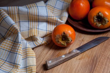 Lezzetli taze hurma meyveleri ve ahşap zemin üzerinde eski model bıçakla yenmeye hazır.