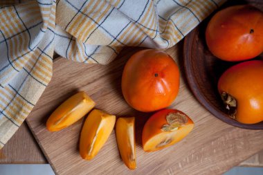 Olgun, lezzetli hurma meyveleri, yarısı ve dilimlenmiş meyveler ahşap zemin üzerinde yenmeye hazır.