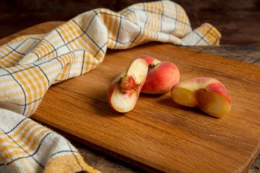 Olgun Çin şeftali meyvelerinin yarısıyla tahta kesmek ya da eski ahşap arka planda sarı mutfak havlusuyla satürn şeftali.