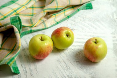 Yeşil mutfak havlusuyla beyaz ahşap arka planda üç taze yeşil elma.