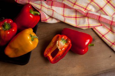 Kırmızı mutfak havlusuyla kırmızı ahşap arka planda kırmızı biber, tatlı dolma biber olarak bilinen tam ve yarı kırmızı ve sarı dolma biber.
