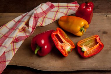 Kırmızı mutfak havlusuyla kırmızı ahşap arka planda kırmızı biber, tatlı dolma biber olarak bilinen tam ve yarı kırmızı ve sarı dolma biber.