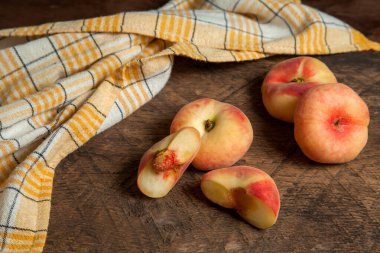 Yarım ve üç tam olgun Çin şeftali meyvesi ya da eski ahşap arka planda sarı mutfak havlusuyla satürn şeftali.