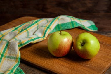Tahta kesme tahtası, ahşap arka planda iki yeşil elma ve yeşil mutfak havlusu.