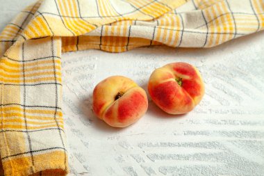 İki olgun Çin yassı şeftali meyvesi ya da eski beyaz ahşap arka planda sarı mutfak havlusuyla satürn şeftali.