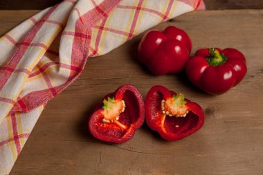 İki tam ve yarısı kırmızı dolma biber (capsicum) tatlı dolma biber olarak bilinir, kırmızı mutfak havlusuyla ahşap arka planda kırmızı biber.