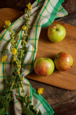 Tahta kesme tahtası, ahşap arka planda yeşil mutfak havlusuyla üç taze elma.