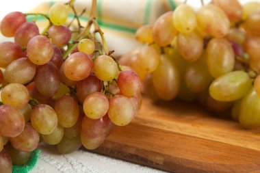 Ahşap kesme tahtasındaki olgun pembe üzümleri yakından izleyin. Beyaz ahşap arka planda yeşil mutfak havlusu olan pembe şarap üzümleri.