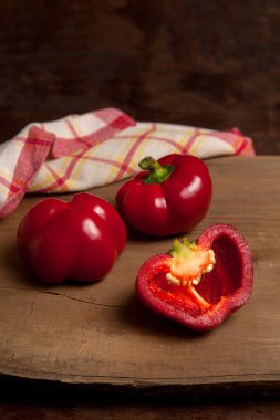İki tam ve yarısı kırmızı dolma biber (capsicum) tatlı dolma biber olarak bilinir, kırmızı mutfak havlusuyla ahşap arka planda kırmızı biber.