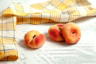 Üç olgun Çin yassı şeftali meyvesi ya da eski beyaz ahşap arka planda sarı mutfak havlusuyla satürn şeftali.