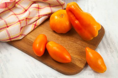 Wooden cutting board with several whole ripe juicy yellow tomatoes and bell pepper on white wooden background with red kitchen towel. Vegetables collection