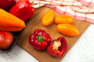 Tahtadaki sebzelerle dolu bir kase. İçinde çeşit çeşit olgun domatesler ve kırmızı mutfak havlusuyla beyaz ahşap arka planda dolma biber var.
