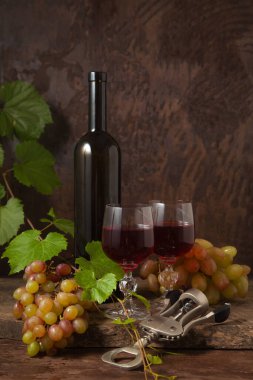 Lezzetli bir alkollü içecek, şarap ve üzüm konsepti. Şarap şişesi, mantar, tirbuşon, kırmızı şarap bardakları ve üzümlü, koyu, ahşap arka planda üzüm yapraklı üzümler.