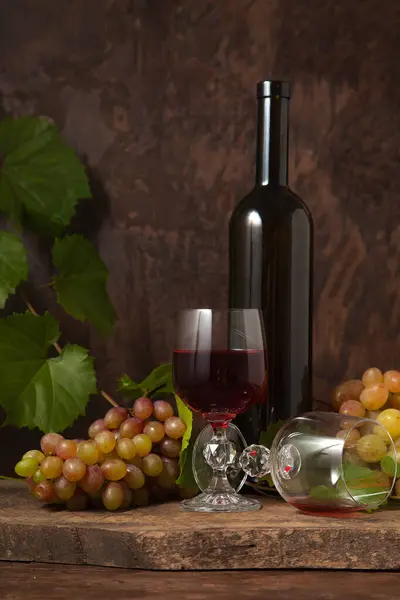 The concept of a delicious alcoholic drink, wine and grapes. Wine bottle, bunch of grapes, empty glass and glass of red wine on dark rustic wooden background with grapes leaves