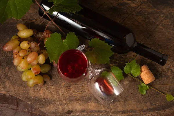 The concept of a delicious alcoholic drink, wine and grapes. Wine bottle, bunch of grapes, empty glass and glass of red wine on dark rustic wooden background with grapes leaves