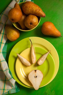 Dilimlenmiş yeşil tabak ve yeşil ahşap arka planda olgun sulu armut meyvesi ve yeşil mutfak havlusu.
