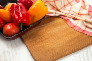 Sebze arkaplan resmi. Tahtadaki sebzelerle dolu bir kase. İçinde çeşit çeşit olgun domatesler ve kırmızı mutfak havlusuyla beyaz ahşap arka planda dolma biber var.