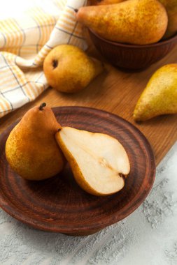 Clay plate with whole and half of ripe juicy pear fruits, wicker basket with pears and yellow kitchen towel on wooden cutting board