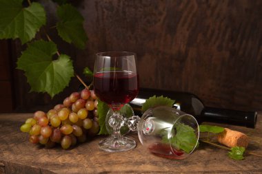 Lezzetli bir alkollü içecek, şarap ve üzüm konsepti. Şarap şişesi, bir demet üzüm, boş bardak ve koyu kırsal ahşap arka planda üzümlü kırmızı şarap.