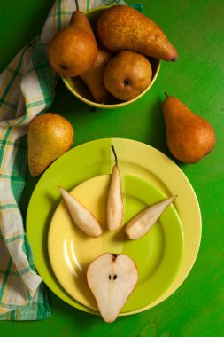 Dilimlenmiş yeşil tabak ve yeşil ahşap arka planda olgun sulu armut meyvesi ve yeşil mutfak havlusu.