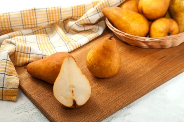 stock image Wooden cutting board with whole and halves of ripe juicy pear fruits, wicker basket with pears and yellow kitchen towel on white wooden background