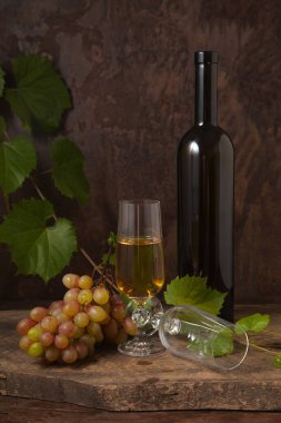 Lezzetli bir alkollü içecek, şarap ve üzüm konsepti. Şarap şişesi, boş bardak ve bir bardak beyaz şarap ve koyu renkli ahşap arka planda üzüm yapraklı bir demet pembe üzüm.