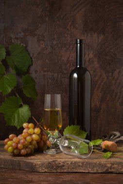 Lezzetli bir alkollü içecek, şarap ve üzüm konsepti. Şarap şişesi, mantar, tirbuşon, boş bardak ve bir bardak beyaz şarap ve koyu sade ahşap arka planda üzümlü pembe üzümler.