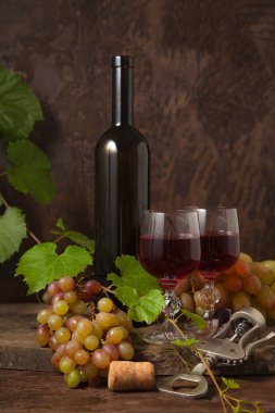 Lezzetli bir alkollü içecek, şarap ve üzüm konsepti. Şarap şişesi, mantar, tirbuşon, kırmızı şarap bardakları ve üzümlü, koyu, ahşap arka planda üzüm yapraklı üzümler.