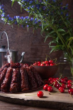 Koyu renk ahşap arka planda kompozisyon - tatlı kirazlı lezzetli çikolatalı pasta, kirazlı kirazlı kiraz kasesi, kaliteli çaydanlık ve güzel mavi çiçekli cam kavanoz.