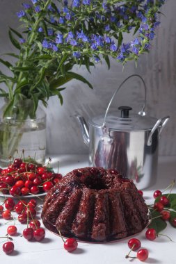 Beyaz arkaplanda kompozisyon - tatlı kirazlı lezzetli çikolatalı pasta, kirazlı beyaz tabak, kaliteli çaydanlık ve güzel mavi çiçekli cam kavanoz.