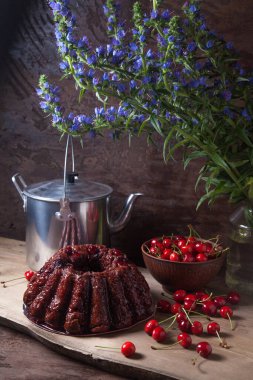 Koyu renk ahşap arka planda kompozisyon - tatlı kirazlı lezzetli çikolatalı pasta, kirazlı kirazlı kiraz kasesi, kaliteli çaydanlık ve güzel mavi çiçekli cam kavanoz.
