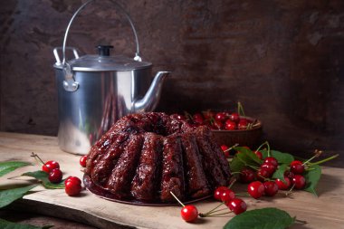 Koyu renk ahşap arka planda kompozisyon - tatlı kirazlı lezzetli çikolatalı pasta, eski moda çaydanlık, kiraz meyveli kiraz kasesi ve kiraz ağacı yapraklı kiraz.