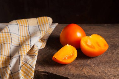 Eski ahşap arka planda kesilmiş, sulu sarı domates ve sarı havlu. Sebze koleksiyonu