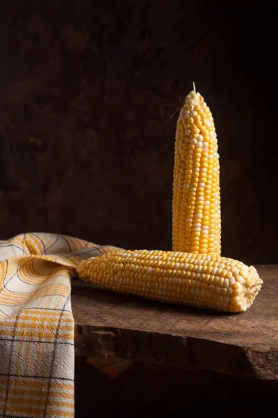 Two ears of ripe sweet corn on wooden background. Cobs with white and yellow grains.