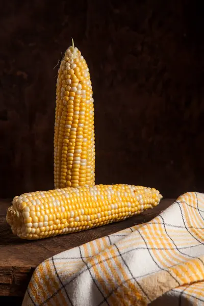 Two ears of ripe sweet corn on wooden background. Cobs with white and yellow grains.