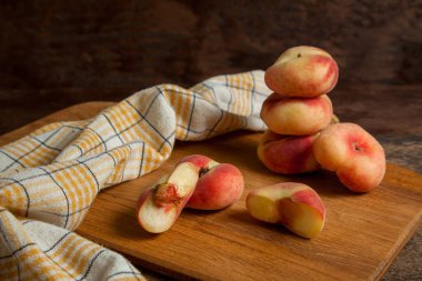 Tahtayı yarımlı kesme tahtası ve bir sürü olgun Çin şeftali meyvesi ya da eski ahşap arka planda sarı mutfak havlusuyla satürn şeftali.