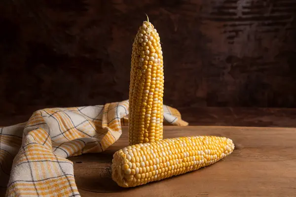 Two ears of ripe sweet corn and yellow towel on vintage wooden background. Cobs with white and yellow grains