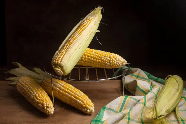 Several ears of ripe sweet corn and green towel on vintage wooden background. Cobs with white and yellow grains. Fresh ears of corn with green leaves on background.