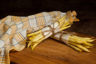 Ahşap zemin üzerinde iki demet ham sarı kayısı ve sarı mutfak havlusu olan tahta kesme tahtası. Fransız fasulyesi ya da Hindistan 'dan String fasulyesi olarak da bilinir. Sebze koleksiyonu.