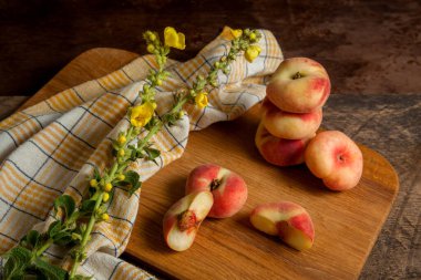 Tahtayı yarımlı kesme tahtası ve bir sürü olgun Çin şeftali meyvesi ya da eski ahşap arka planda sarı mutfak havlusuyla satürn şeftali.